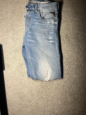 Replay ljusblå jeans Grover - Säljer ett par snygga ljusblå jeans från Replay, modell Grover. Jeansen har en klassisk femficksdesign, slitna detaljer och en tvättad look som ger en avslappnad vibe. Tillverkade i bomull med en skön passform och Replay-logga vid fickan.