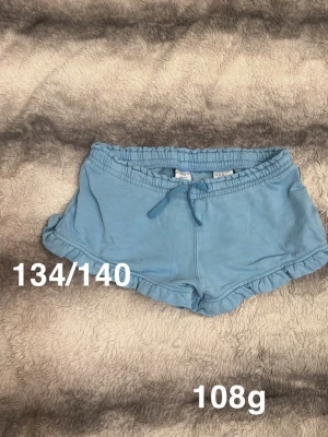 Blå shorts med snörning - Säljer ett par ljusblå shorts med snörning i midjan och volangkant. perfekta för varma dagar. Passar dig som gillar en avslappnad och sportig stil.🌸 Fint använt skick. Storlek 134/140