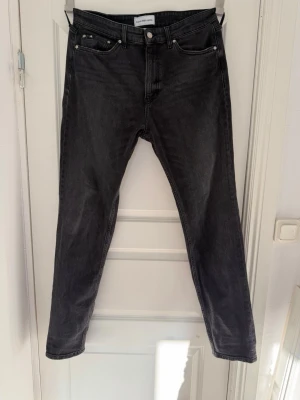 Svarta jeans från Calvin Klein - Snygga svarta jeans från Calvin Klein med klassisk femficksmodell och raka ben. Jeansen har diskreta sömmar och en liten CK-logga bak i midjan. Tillverkade i mjuk denim som ger en skön passform och stilren look.  W32 L34