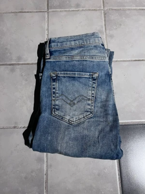 Blå jeans från Replay - Snygga blå jeans från Replay med klassisk femficksdesign och slitna detaljer. Jeansen har en ljus tvätt och raka ben. Perfekta för en avslappnad och trendig look.