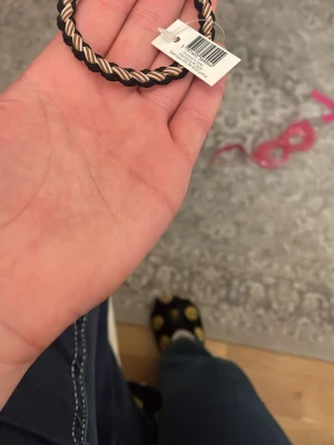 Flätad hårsnodd svart och beige - Säljer en snygg flätad hårsnodd i svart och beige. Hårsnodden har en tvinnad design och är gjord av elastiskt material som passar perfekt för att hålla håret på plats. Enkel att matcha med olika outfits och superpraktisk att ha i väskan.