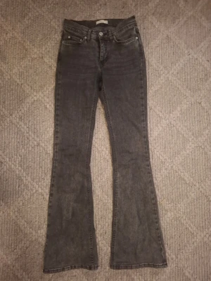 Grå/ svartabootcut jeans med utsvängda ben - Säljer ett par grå/svarta bootcut jeans med utsvängda ben och klassisk femficksmodell. Jeansen har normal midja och är lite stretchiga. Lappen på baksidan har spurckit men går att ta bort. Pris kan diskuteras💗