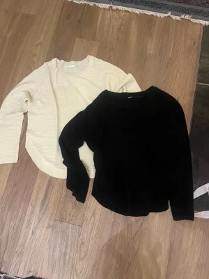 Svart och vit stickad tröja - Två stickade tröjor i klassisk modell, en i svart och en i vit. Båda har rund halsringning och långa ärmar. Perfekta att matcha med jeans eller kjol för en stilren look.