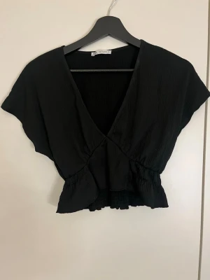 Svart croppad omlottopp - Snygg svart croppad omlottopp med v-ringning och korta ärmar. 