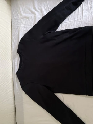 Sweatshirt från Sail Racing - En stilren svart sweatshirt från Sail Racing med rund halsringning och diskret logga på ärmen. Tröjan har långa ärmar och är gjord i mjukt bomullsmaterial. Perfekt för en avslappnad och snygg look.