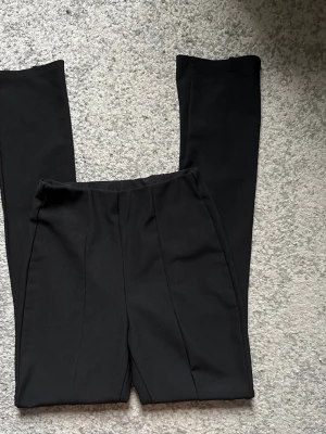 Svarta raka kostymbyxor - Säljer ett par svarta kostymbyxor med rak passform och pressveck framtill. Byxorna har hög midja och är sydda i ett slätt, vävt material som ger en stilren look. Perfekta till en dressad outfit.