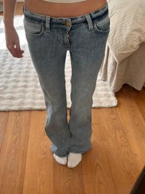 Blå bootcut jeans med låg midja - Säljer ett par ljusblå bootcut jeans med låg midja och klassisk femficksdesign. Jeansen har slitna detaljer och är tillverkade i denim med en lätt tvättad look. Perfekta för en avslappnad och trendig stil.