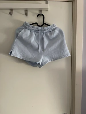 Ljusblåa shorts med snörning - Säljer ett par ljusblåa shorts med elastisk midja och snörning framtill. Shortsen har en avslappnad passform och är tillverkade i mjukt bomullsmaterial, perfekta för varma dagar.