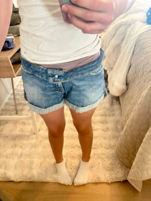 Blå jeansshorts med upprullad kant - Snygga blå jeansshorts med upprullad kant och klassiska fickor fram och bak. Shortsen har låg midja och är perfekta för varma dagar. De är gjorda i bomull och har en avslappnad passform som ger en chill vibe.