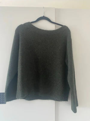 Mörkgrön stickad tröja - Mysig mörkgrön stickad tröja med rund halsringning och långa ärmar. Tröjan har en avslappnad passform och är tillverkad i ett mjukt, luddigt material som känns skönt mot huden. Perfekt för kyliga dagar.