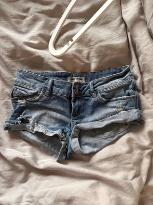 Blå denimshorts från Tally Weijl - Säljer ett par blå jeansshorts från Tally Weijl med väldigt låg midja och slitna detaljer. Så snygga! 
