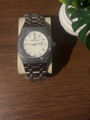 Audemars Piguet Royal Oak  - Snygg Audemars Piguet Royal Oak klocka i silver med ikonisk åttakantig boett och vit urtavla. Klockan har länkarmband i rostfritt stål och tydliga indexmarkeringar. Perfekt accessoar för dig som gillar klassisk och stilren design. Priset kan diskuteras!