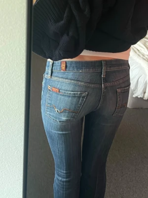 Blå low waist jeans från 7 for all mankind  - Säljer ett par blå low waist jeans från 7 for all mankind, med klassiska kontrastsömmar och broderade fickor bak. Jeansen har smal bootcut passform och detaljerade nitar. Perfekta för dig som gillar en avslappnad men ändå trendig look. Dessa är såå snygga men tyvärr för små för mig. Strl 25 i midjan. Jag har haft stor användning av jeansen men de är fortfarande i bra skick. Finns ett litet knappt märkbart hål på höger ficka. Denna typen av modell på jeans finns inte längre att köpa i butik.