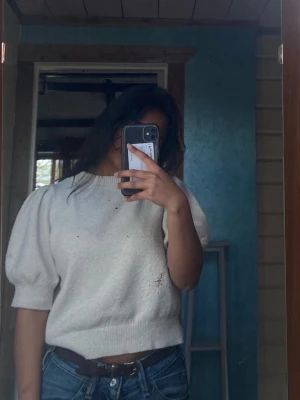 Vit puffärmad stickad tröja - Säljer en vit stickad tröja med puffärmar och ribbad nederkant. Tröjan har en croppad passform och kortare ärmar som ger en trendig look. Perfekt att matcha med jeans eller kjol för en avslappnad stil.