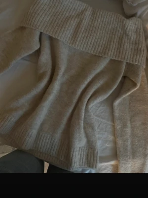 Beige off shoulder stickad tröja - Säljer en beige stickad tröja med bred ribbad off shoulder-krage. Tröjan har långa ärmar och ribbade muddar vid ärmslut och nederkant. Mjuk och skön, perfekt för kyliga dagar. Passar snyggt till jeans eller kjol. Aldrig aldrig använt bara testat till denna bild