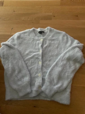 Ljusblå fluffig kofta från Esmara - Mysig ljusblå kofta från Esmara med fluffig textur och rund halsringning. Koftan har långa ärmar och stängs med vita knappar framtill. Perfekt för lager på lager och ger en soft look till din outfit.