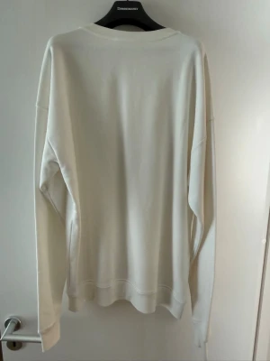 Vit sweatshirt från Moschino - Säljer en stilren vit sweatshirt från Moschino Couture! Milano. Tröjan har en klassisk rund halsringning, långa ärmar och ribbade muddar. Tillverkad i mjukt material som känns skönt mot huden. Perfekt för dig som gillar minimalistisk och exklusiv design.