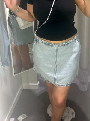 Ljusblå jeanskjol med dragkedja - Trendig ljusblå jeanskjol i kort modell med synlig dragkedja framtill och klassiska sömmar. Kjolen har en rak passform och är tillverkad i denim, perfekt att matcha med en enkel topp eller hoodie.