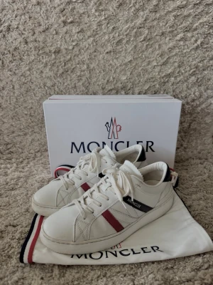 Vita Moncler skor - Vita Moncler skor i storlek 43, köpta för ett år sedan men inte kommit till användning. Köpta på Care of Carl för 6000kr. Inga tecken på slitage (skriv för fler bilder). Box, dustbag, kvitto m.m ingår såklart vid köp. Tveka inte på att höra av dig vid minsta fundering. 