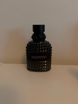 Valentino born in roma edt parfym 50ml - Säljer en Valentino parfym i en cool svart flaska med nitar och text i rosa. Flaskan rymmer 50 ml och har en unik, lyxig design i glas med struktur. Perfekt för dig som gillar exklusiva dofter och snygga detaljer på parfymhyllan. Det är lite mindre än hälften kvar i flaskan.