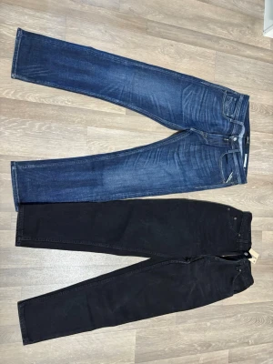Blå och svarta raka jeans - Två par jeans säljer båda tillsammans. ett par i klassisk blå denim med raka ben och ett par i svart denim med hög midja och raka ben. Båda har femficksdesign och knappgylf. Perfekta för en avslappnad och stilren look. Mörkblåa: W29 L30 plus de är lite sliten där bak, svarta jeansen: W28 L32, helt helt nya! 