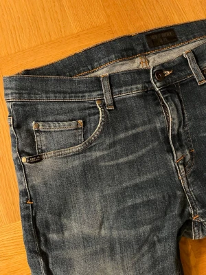 Tiger of Sweden jeans  - Passar W32-W33. Säljer ett par blå slim fit jeans från Tiger of Sweden med snygga slitningar och klassisk femficksmodell. Jeansen har orangea sömmar och är tillverkade i mjukt denimtyg som sitter riktigt bra. Perfekta för dig som gillar en modern och stilren look.