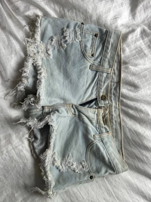 Ljusblå fransiga jeansshorts C&J jeans  - Säljer ett par ljusblå jeansshorts från C&J jeans med fransiga kanter och slitna detaljer både fram och bak. Klassisk femficksmodell med knapp och dragkedja. Perfekta för varma dagar och en avslappnad look. Jag köpte de begagnat men nu passar de inte längre. 💕