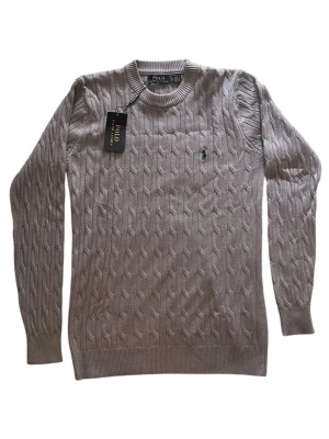 Grå kabelstickad Polo Ralph Lauren - Snygg Grå kabelstickad tröja från Polo Ralph Lauren med klassisk rund halsringning och broderad logga på bröstet. Helt ny och oanvänd 