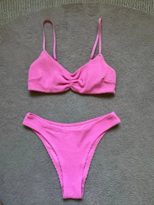 Snygg rosa ribbad bikini med scrunchdetalj - Säljer en superfin barbie rosa bikini med ribbad textur💞Överdelen har smala justerbara axelband och scrunchdetalj framtill, medan underdelen är snyggt skuren för en trendig look! Perfekt för dagar på stranden eller poolen😍Mjukt och bekvämt material. Toppen har vaddering som kan tas ut! Använd ca 3 gånger, inga fläckar på underdelen. Hör av vid frågor, pris diskuterbart❤️