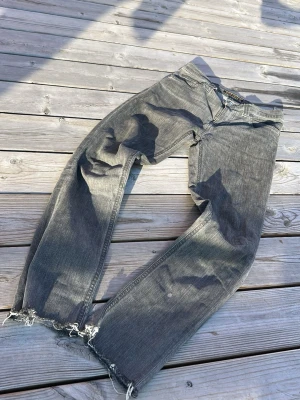 Grå raka jeans med slitna benslut - Säljer ett par grå jeans med rak passform och slitna, fransiga benslut. Jeansen har klassisk femficksdesign och är tillverkade i denim. Perfekta för en avslappnad och trendig look.klippta till L 30/32
