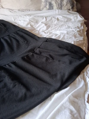 Svart långkjol - En svart långkjol med resår i midjan. Kjolen har en lätt strukturerad yta och ett avslappnat fall. Perfekt för dig som gillar enkel och stilren design.