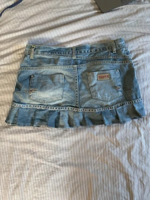 Blå jeanskjol med volangkant - Säljer en blå jeanskjol med volangkant längst ner och klassiska fickor både fram och bak. Kjolen har bälteshällor och en snygg tvättad denimlook. Perfekt för dig som gillar en avslappnad men trendig stil. har sytt denna själv 