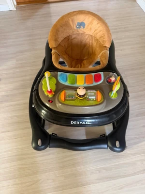 Gåstol med leksaker från Deryan - Rolig gåstol i svart och beige med mjuk sits och färgglada aktivitetsleksaker på brickan. Sitsen har ett elefantmotiv och stolen har flera knappar och snurrande delar för lek. Perfekt för små barn som vill utforska och röra sig hemma.