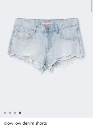 Ljusblå lågmidjade jeansshorts - Säljer ett par ljusblå denimshorts från Ginajeans med låg midja och fransig, rå kant. Shortsen har klassisk femficksdesign och slitna detaljer framtill för en avslappnad look. Perfekta till sommaren!