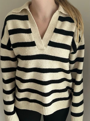 H&M-tröja S - beige, svart - Tröja från H&M i ett beige- och svartrandigt mönster. Tröjan har en v-ringning med krage samt ribbstickade muddar. Mycket bra skick utan synliga tecken på användning. Tröjan är gjord i akryl, polyester och ull.