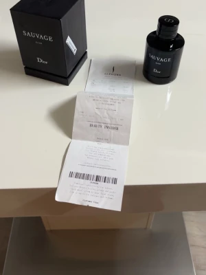 Dior Sauvage Elixir 100ml - Dior Sauvage Eau de Parfum med elegant svart glasflaska och matchande svart kartong. Flaskan har en stilren, rund form med silverdetaljer och tydlig Dior-logga på locket. En klassisk och maskulin doft som ger exklusiv känsla. Perfekt för dig som gillar lyxiga parfymer. Med kvitto!