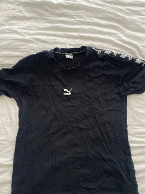 Svart Puma t-shirt med logga - Svart t-shirt från Puma med vit logga på bröstet och tryckt Puma-text längs axlarna. Klassisk passform och rund halsringning.