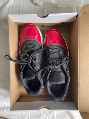 Svarta och röda Air Jordan 11 cmft low sneakers - Snygga sneakers med svart mesh och lackdetaljer i rött. Skorna har vita och röda sulor med coolt mönster undertill. Klassisk snörning och ikonisk design som sticker ut. Perfekta för dig som vill ha något unikt och sportigt i garderoben.
