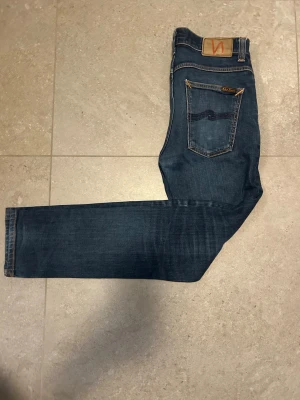 Mörkblå   Nudie jeans  - Säljer ett par klassiska blå jeans från Nudie Jeans med smal passform och snygga slitningar. Modellen är grim Tim och är i mycket bra skick storlek 31/32. Ifall ni har några frågor är det bara att hojta till!!!  Priset är ej hugget i sten!!