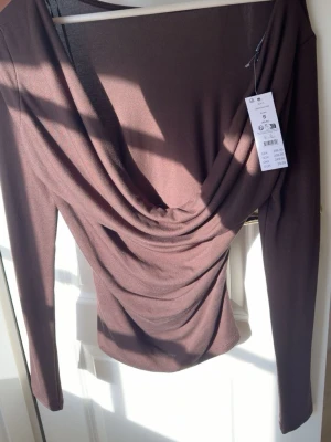 Brun långärmad topp med drapering - Snygg brun långärmad topp med draperad front och rund halsringning. Som är i ett mjukt och stretchigt material perfekt till sommar. Perfekt för dig som vill ha en stilren men ändå unik look. Pris kan diskuteras vid snabbt köp 