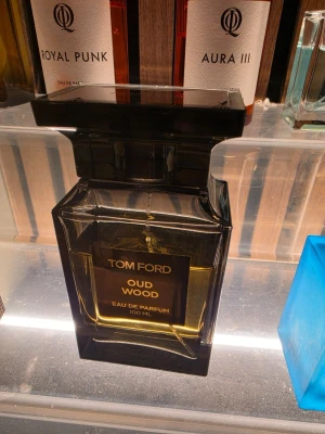 Tom Ford Oud Wood Eau de Parfum - Tom Ford Oud Wood Eau de Parfum 100 ml i en elegant, mörkbrun glasflaska med svart fyrkantigt lock. Flaskan har en lyxig och stilren design med guldtext på etiketten. En exklusiv doft som sticker ut med sin unika och djupa karaktär. Presentation finns köpt Nk 
