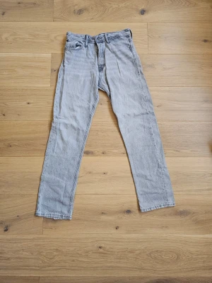Grå raka jeans från Jack & Jones - Säljer ett par gråa raka jeans från J&J med klassisk femficksdesign och knappgylf. Jeansen har en vintagekänsla. Passar perfekt till en avslappnad streetwear-look.