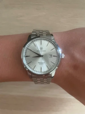 Pablo Raez silverfärgad klocka - Stilren klocka från Pablo Raez med silverfärgat armband i metall och en ljus urtavla med solstrålemönster. Klockan har datumvisning och klassisk design som passar till många stilar. Perfekt accessoar för dig som gillar en clean look.