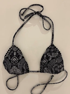 Svart bikiniöverdel från BikBok - Snygg trekantsbikini i svart med vitt paisleyinspirerat mönster och dekorativa små bollar längs kanterna. Knytband i nacken och ryggen för justerbar passform. Endast använd en gång 💙
