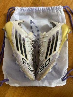 Adidas F50 fotbollsskor vit/guld 42 2/3 - Säljer ett par Adidas F50 fotbollsskor i storlek 42 2/3 i fg/ag. Skorna är i nyskick använda 2 träningar och jag säljer pga de är för små. Hör av dig om du har några frågor.