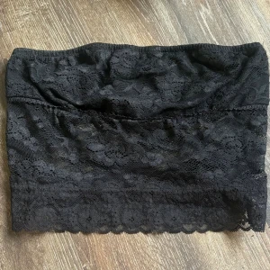 Svart spets tubtopp - Snygg svart tubtopp i spets med blommigt mönster. Toppen är axelbandslös och har en feminin, croppad passform. Perfekt att styla under en skjorta eller till höga jeans.