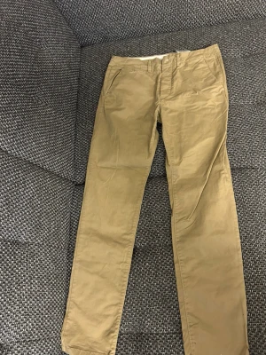 Beiga chinos från Jack & Jones - Snygga beiga chinos från Jack & Jones med klassisk rak passform och diskreta sidofickor. Perfekta för en stilren och avslappnad look. Tillverkade i mjukt bomullstyg med bälteshällor och dragkedjegylf.