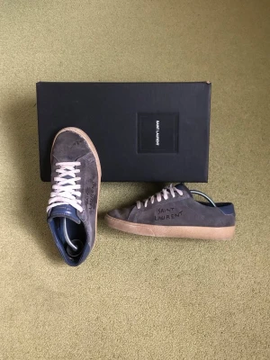Yves Saint Laurent skor - Säljer ett par väl använda mörkblåa YSL skor! Storlek: 40,5 men sitter 41/41,5, jag har vanligtvis storlek 42 och det har funkat för mig. Modell: SL06 Low Top Sneaker (Bild 7) Hela under och passar bra för dig som vill hitta äkta billiga designer skor. Gå till en skomakare hade inte varit så fel. Bild 5 för att se defekter, utöver de är skorna i ett okej skick. Skor och låda tillkommer. Nypris: 7000kr+ Mitt pris: 999kr då de är mycket använda och skicket inte är på top, skriv vid funderingar!