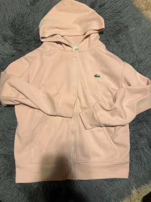 Ljusrosa zip hoodie från Lacoste - Jag har just nu en rosa och en ljusblå Lacoste zip up hoodie för salu, Jag har kvitto på båda, den rosa kostade 1400 samt den blåa. Dem är perfekta just nu inför sommaren pågrund av färgen