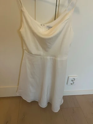 Vit satin-klänning från Princess Polly - Säljer en vit klänning från Princess Polly i satinliknande material. Klänningen har tunna axelband, lätt draperad urringning och en något utställd kjol. Dragkedja i ryggen för enkel påklädning. Perfekt för dig som gillar minimalistisk och stilren look.